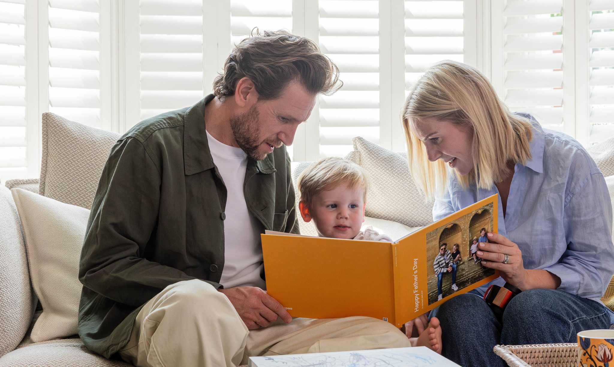 A mother and young child present the child's father with a Father's Day-themed Photo Book