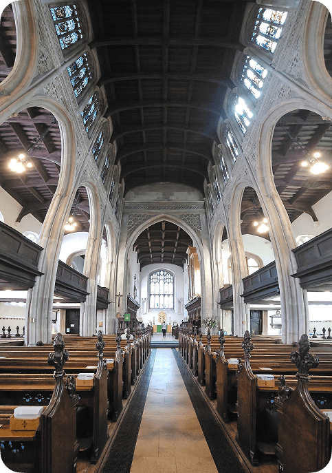 Interior of a historic church with wooden pews, vaulted arches, and stained glass windows, leading to an altar at the far end.