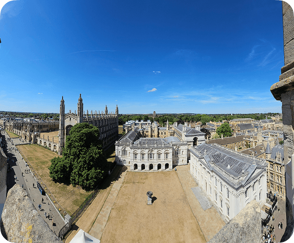 Panoramic view of historic university buildings with a large courtyard, lush greenery, and a clear blue sky.
