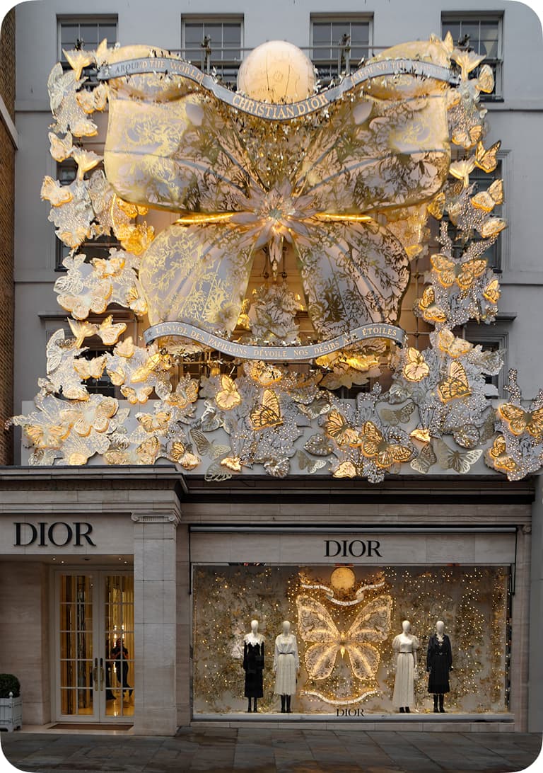 Dior storefront adorned with elaborate butterfly-themed decorations and golden lights, featuring mannequins in elegant attire.