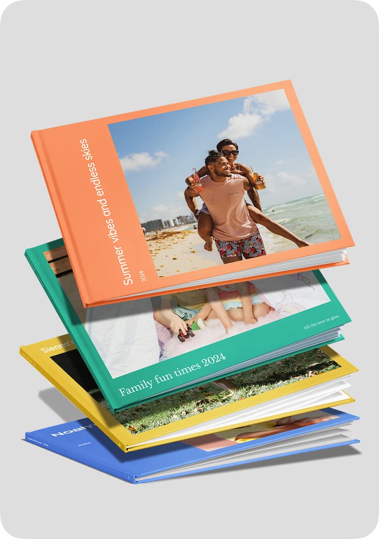 A stack of colorful photo books with various covers, including a beach scene, a family, and a green cover titled "Family fun times 2024."