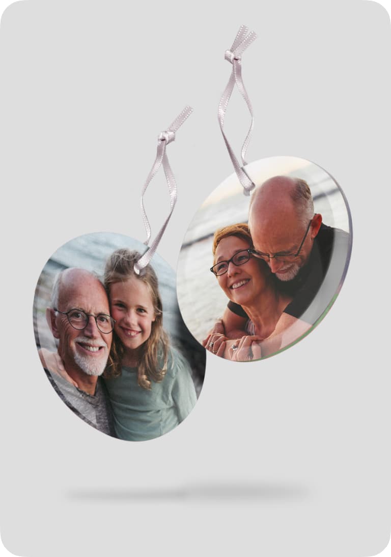 Two round photo ornaments with ribbon ties, featuring a smiling elderly man with a young girl, and a couple embracing by the sea.