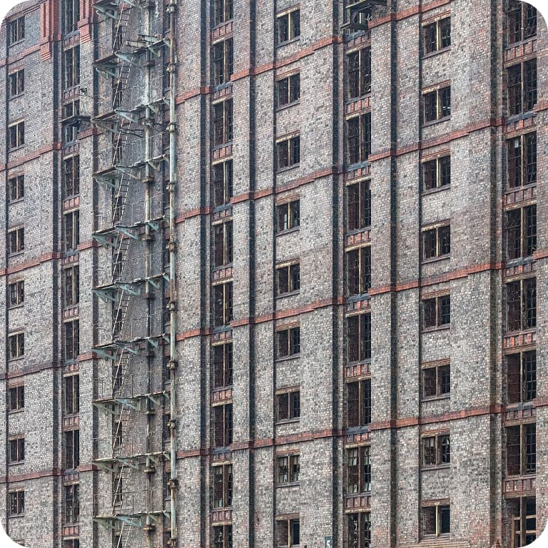 Close-up of a large brick building with numerous windows and an external metal staircase running vertically along the side.