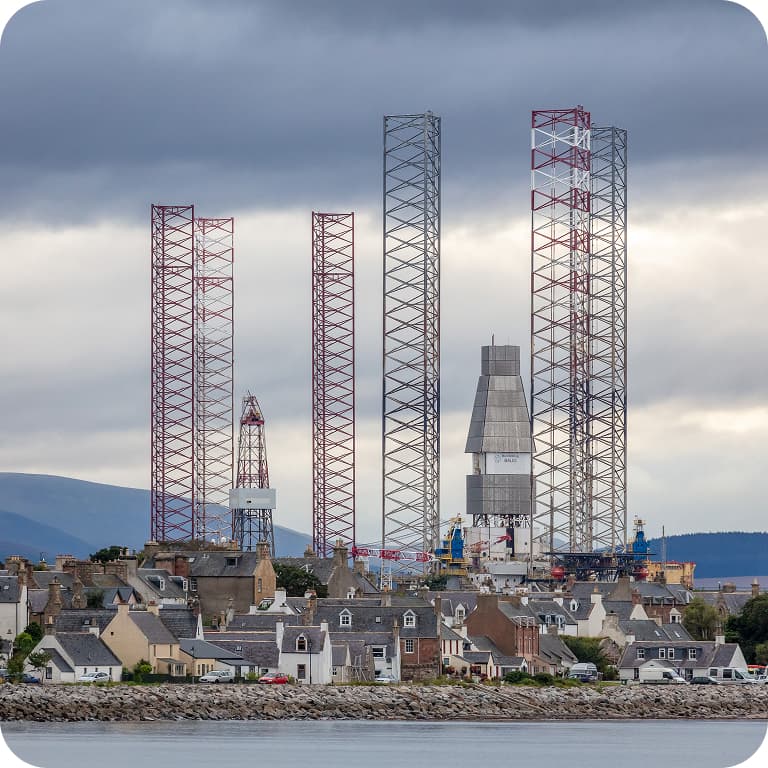 Coastal town with tall industrial structures and cranes in the background under a cloudy sky.