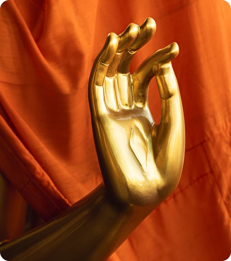 Gold statue hand forming an "OK" gesture (mudra) against orange draped fabric background.
