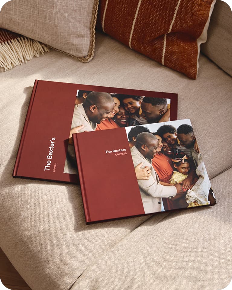 Two red photo albums labeled "The Baxter's" with a family picture on a beige couch, next to a brown and white pillow.