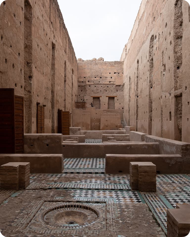 Ancient stone courtyard with patterned tile floor, surrounded by tall, weathered walls featuring small openings and wooden doors.
