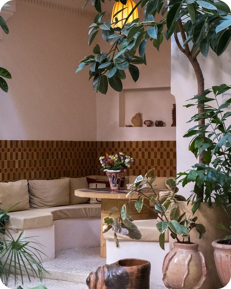 Cozy indoor patio with a corner seating area, potted plants, and a small round table adorned with a colorful vase of flowers.